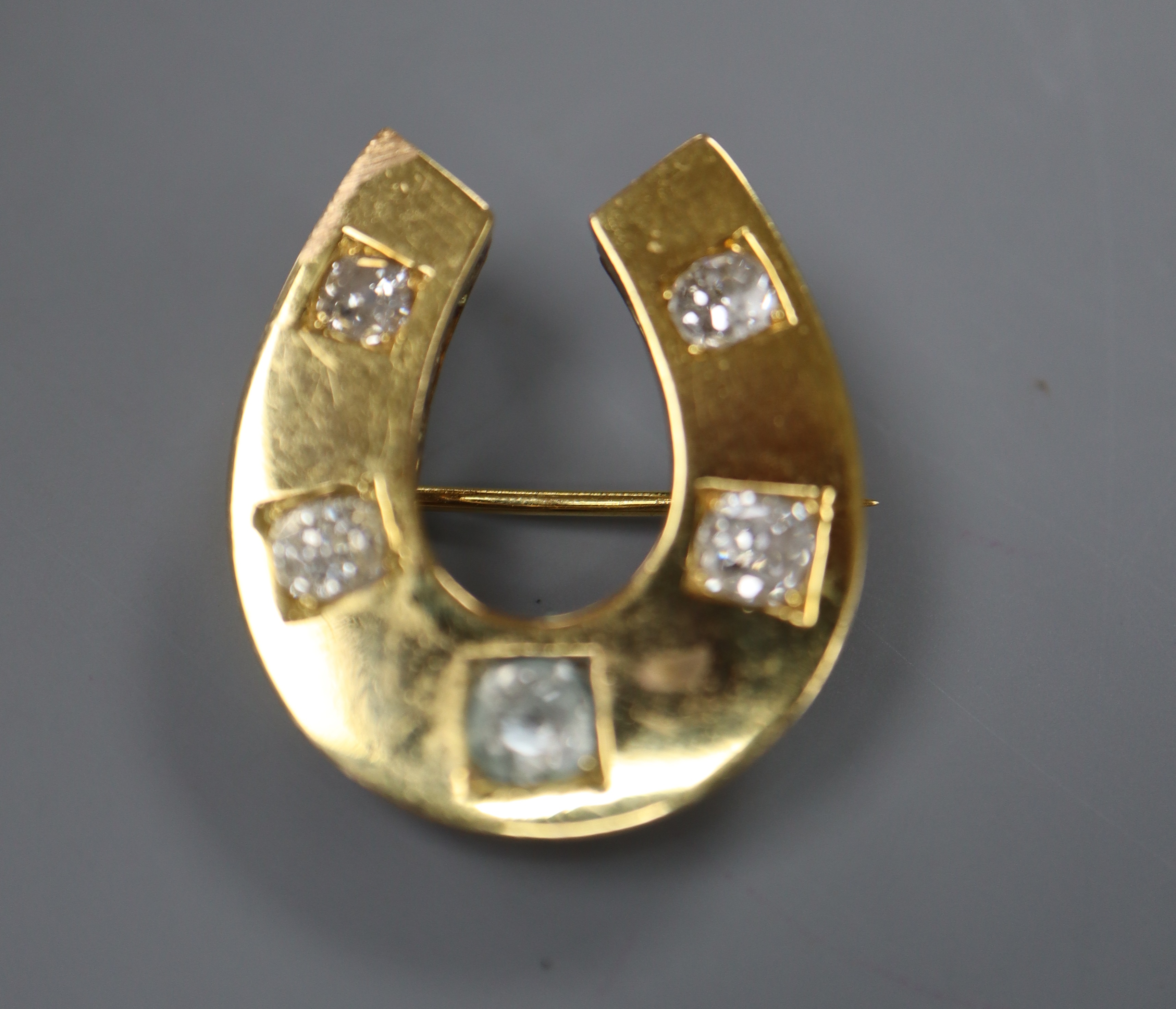 A yellow metal and five stone round cut diamond set horseshoe pendant brooch, 26mm, gross 8.8 grams.